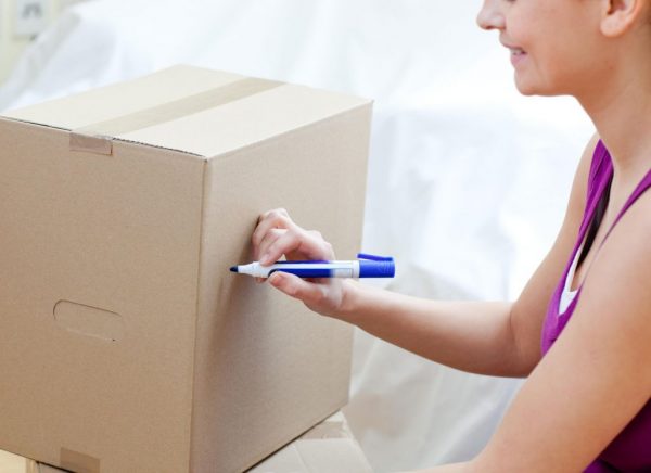 a woman writing on a cardboard box to label it for a move