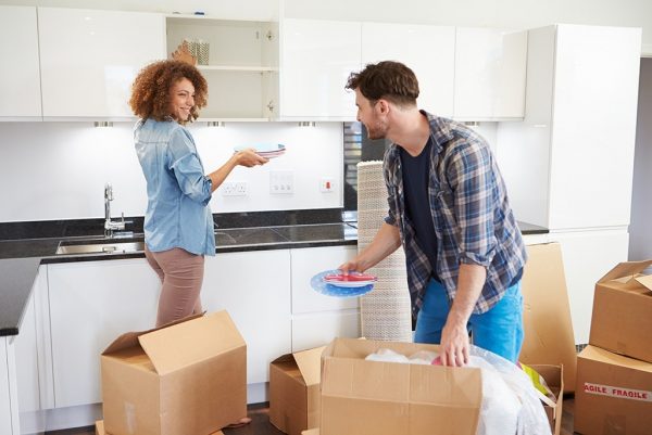 Couple Moving Into New Home And Unpacking Boxes Smiling At Each Other