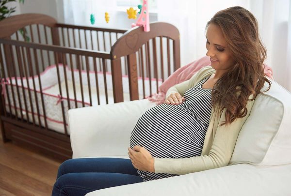an expecting mother sitting down by the crib