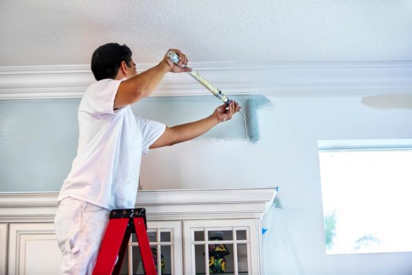 A man using a long paintroller to paint the walls