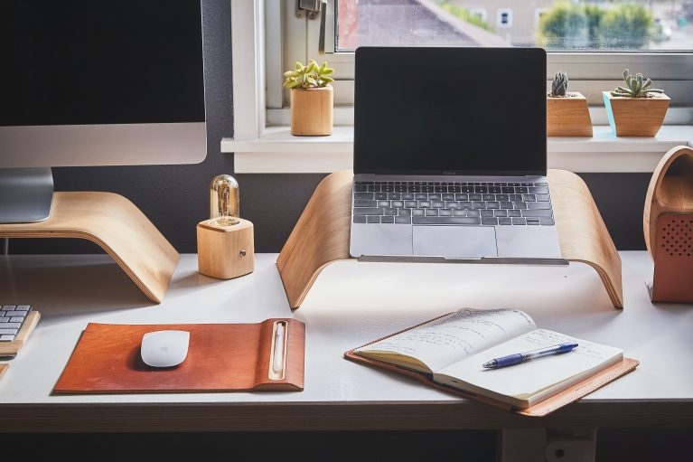 Home office desk set up with laptop and wooden/brown set up on a white desk.